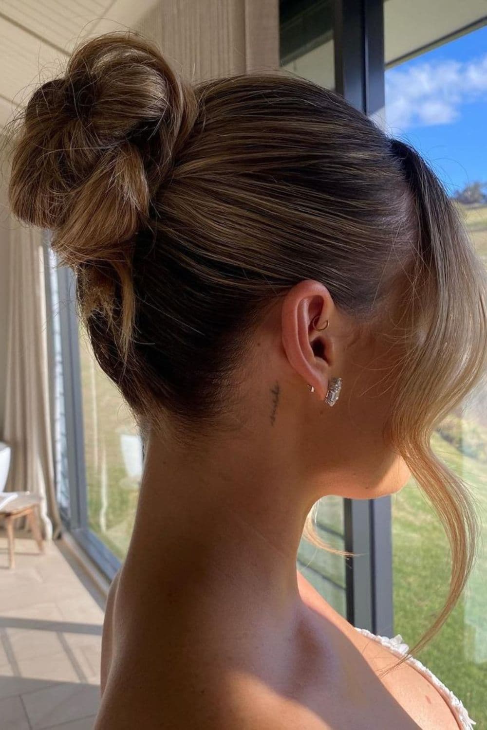 Side view of a woman with a high bun with bangs.
