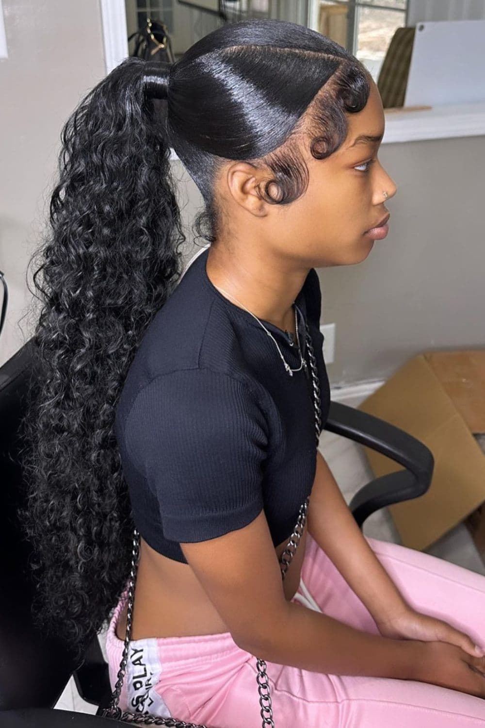 Side view of a woman sitting in a salon with a high ponytail weave.