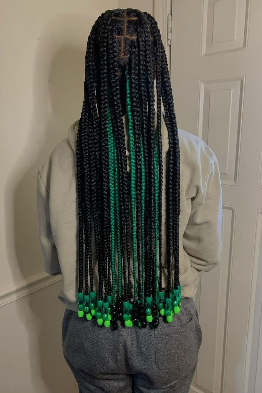 A woman standing with a black and green knotless braid with green beads.