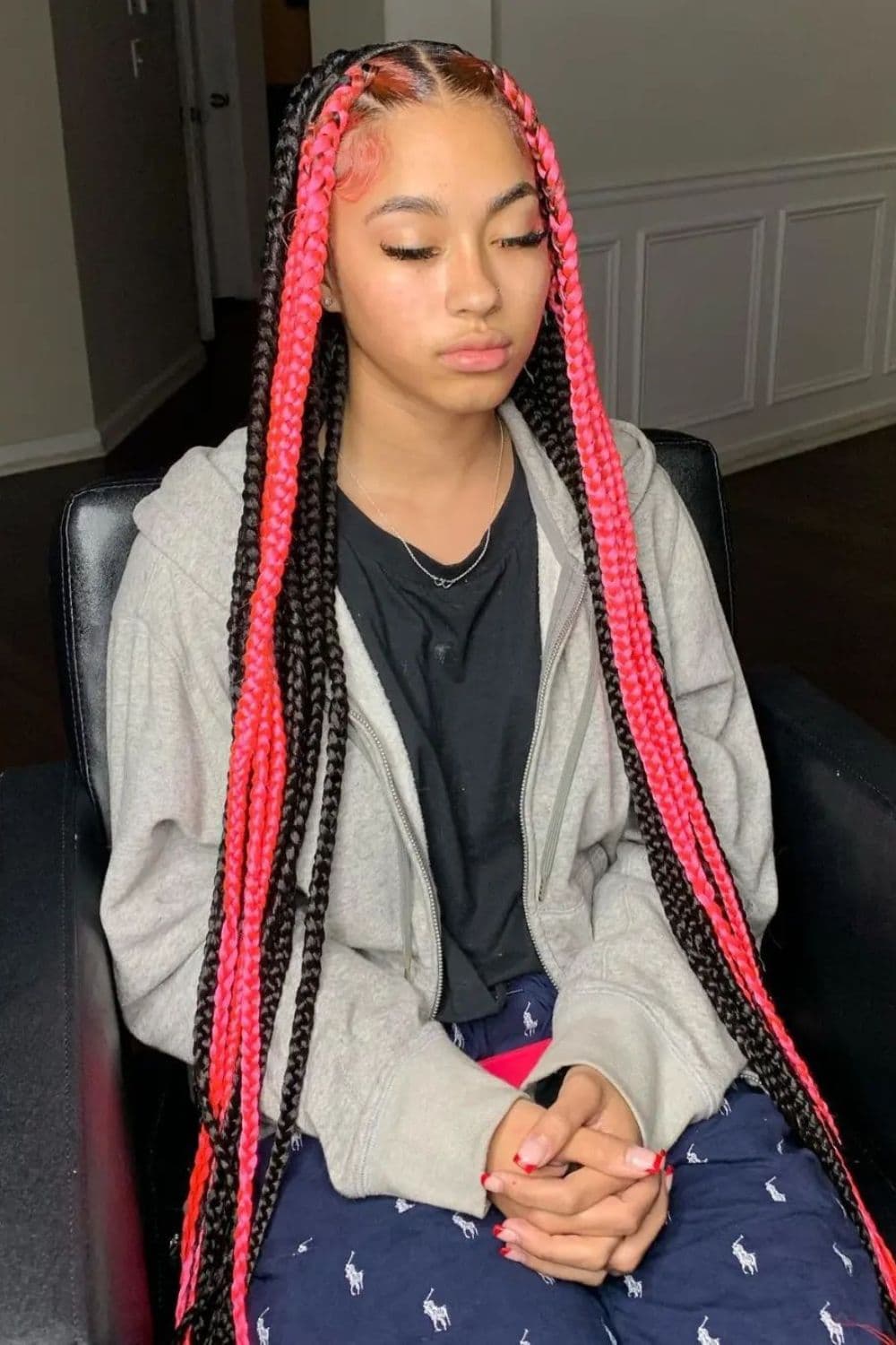 A woman sitting on a chair with black and pink knotless braids.