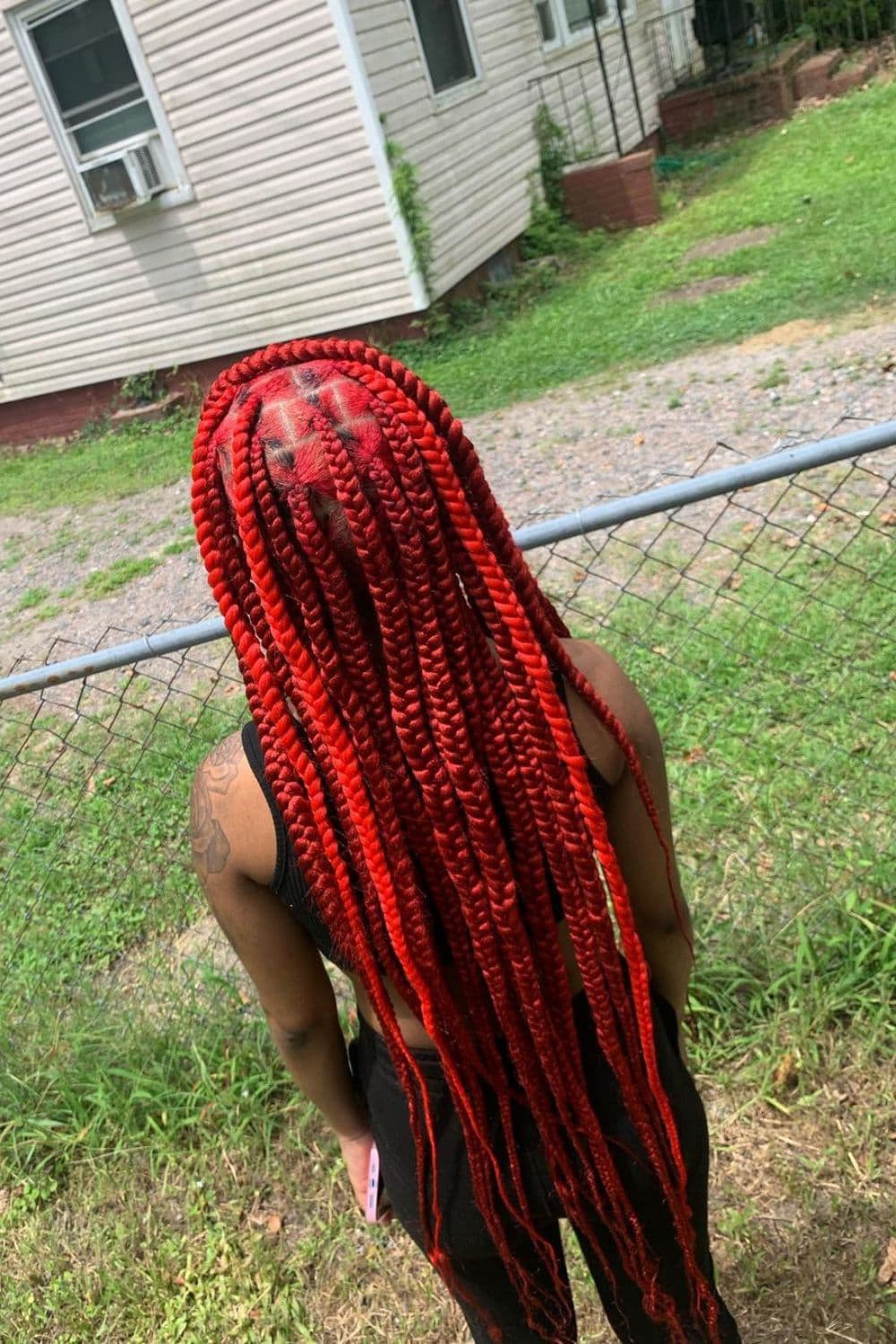 Back of a woman standing on the grass with large red knotless braids.