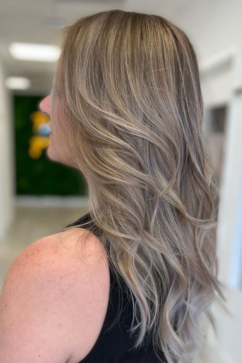Side view of a woman with blonde balayage and layered beach waves.