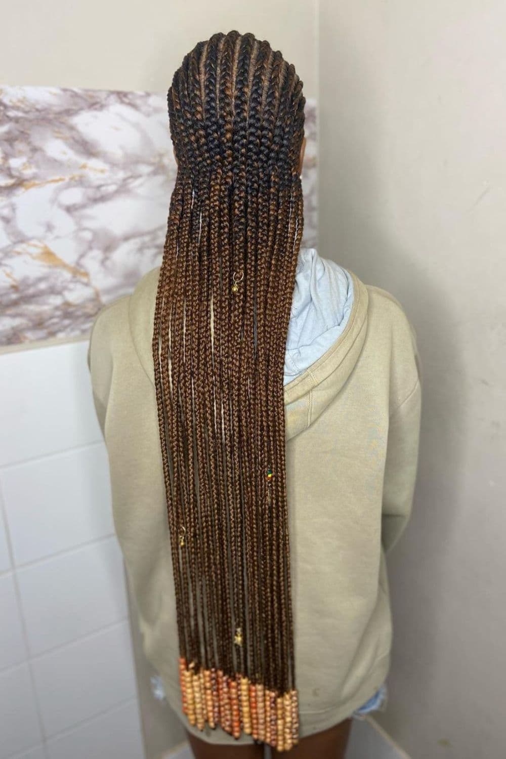 A woman wearing a sweater with brown long cornrows with beads.