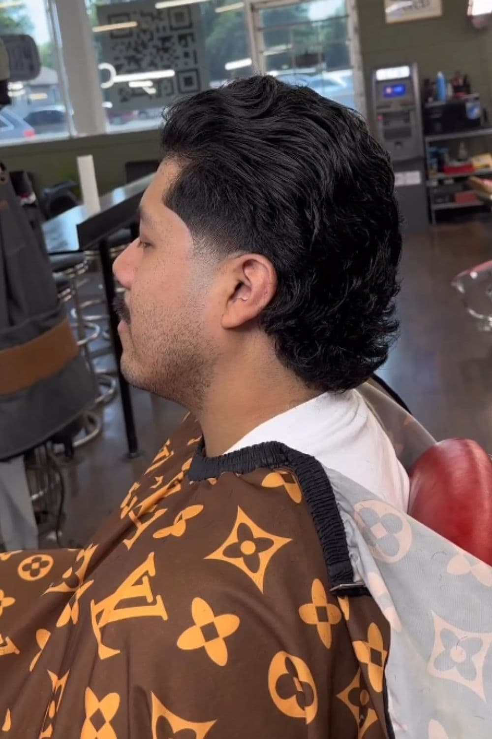 Side view of a man sitting in a barber shop with long hair low taper fade.