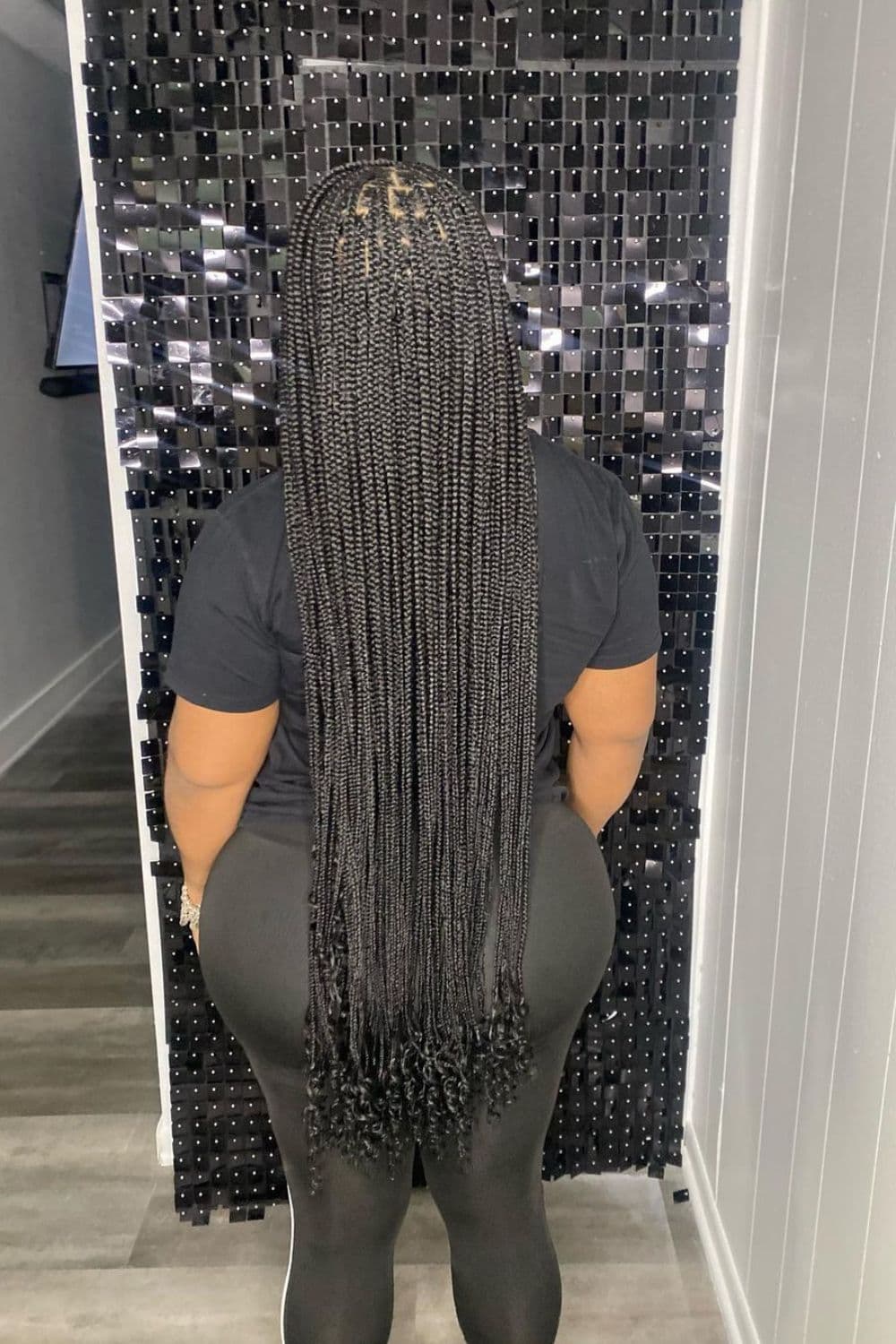 Back of a woman standing with long black medium knotless braids with curly ends.