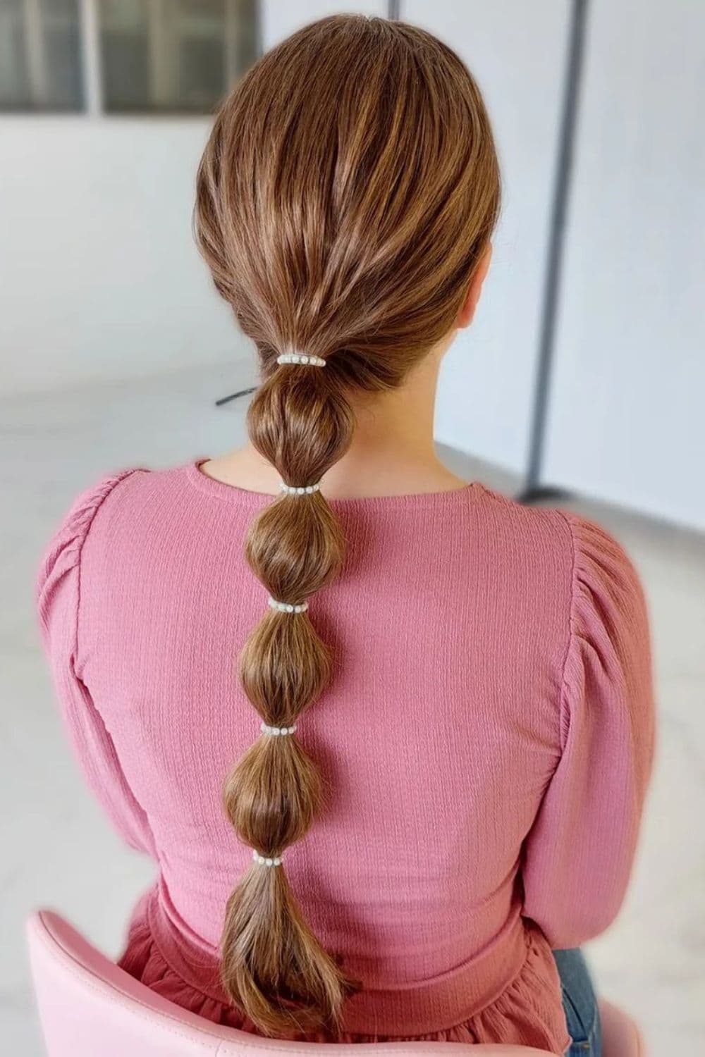 A woman in a pink blouse with a brown low bubble ponytail.