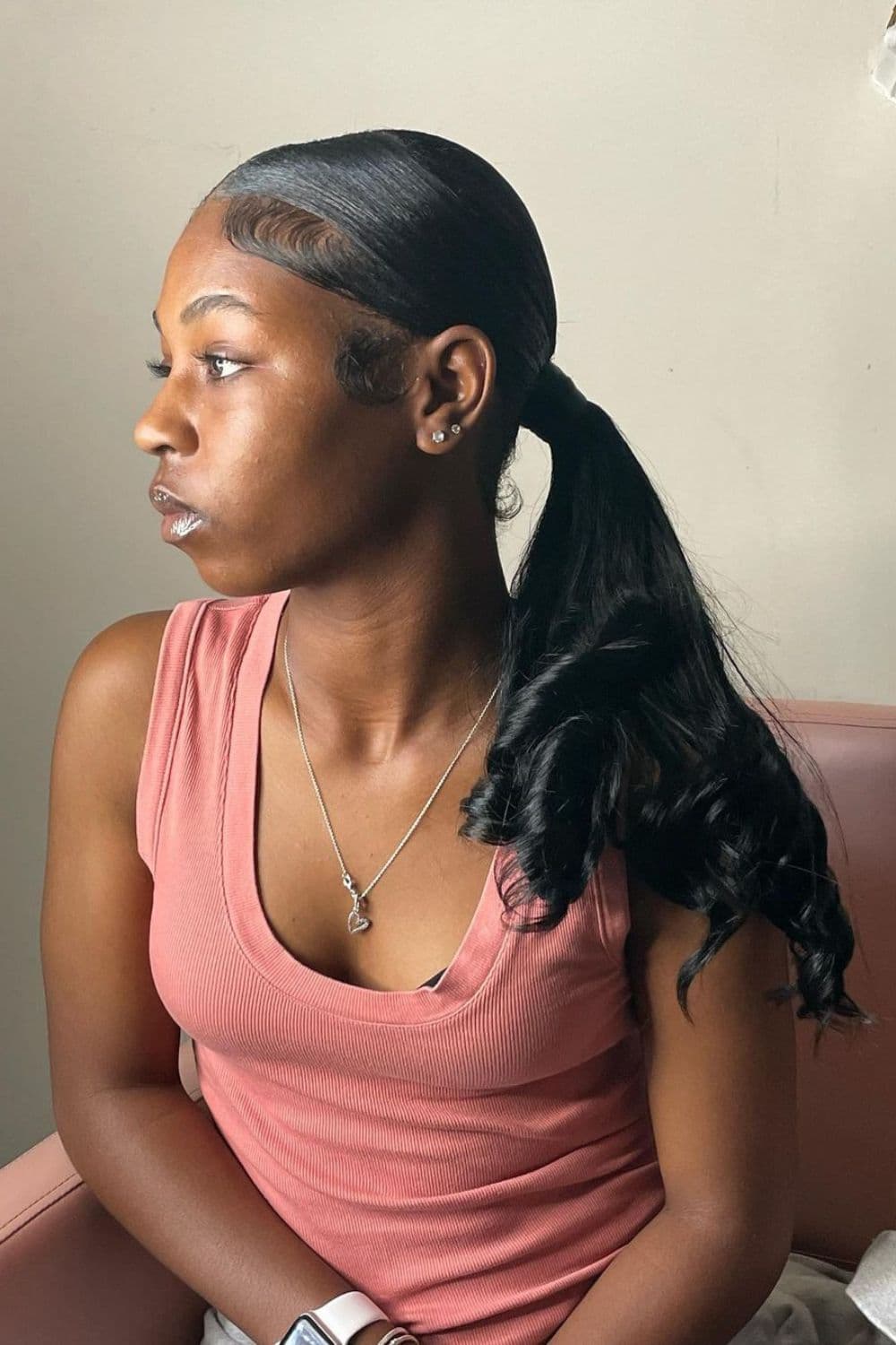 Side view of a woman sitting on a chair with a black low ponytail.