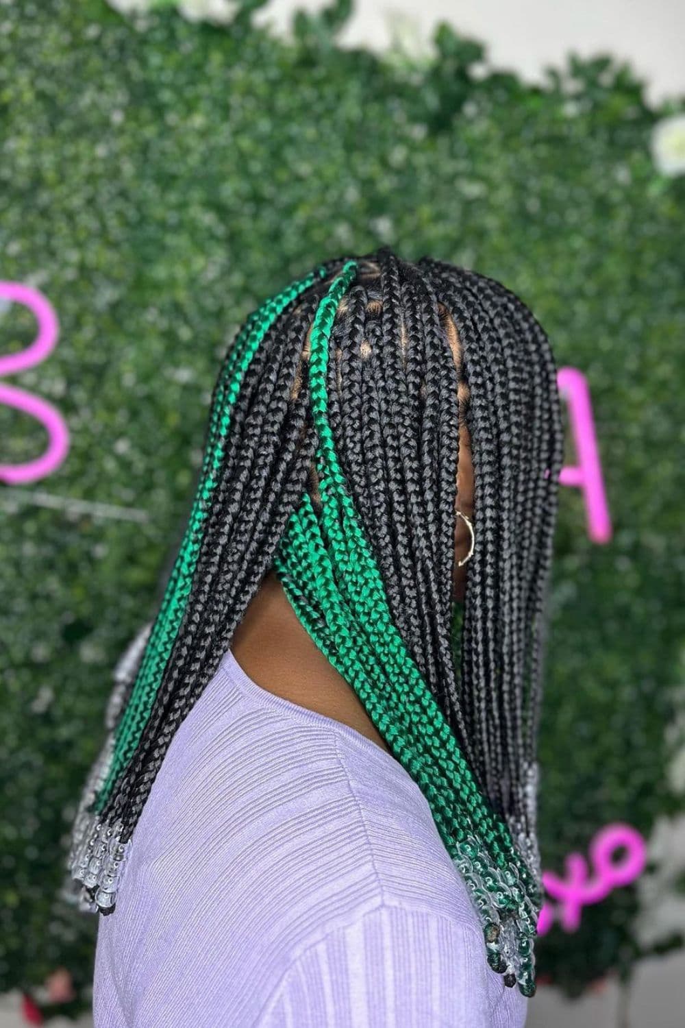 Side view of a woman with green and black medium box braids with beads.