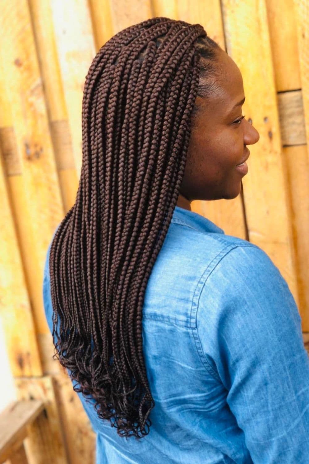 Side view of a woman in jeans-colored long sleeves with brown medium box braids with curly ends.