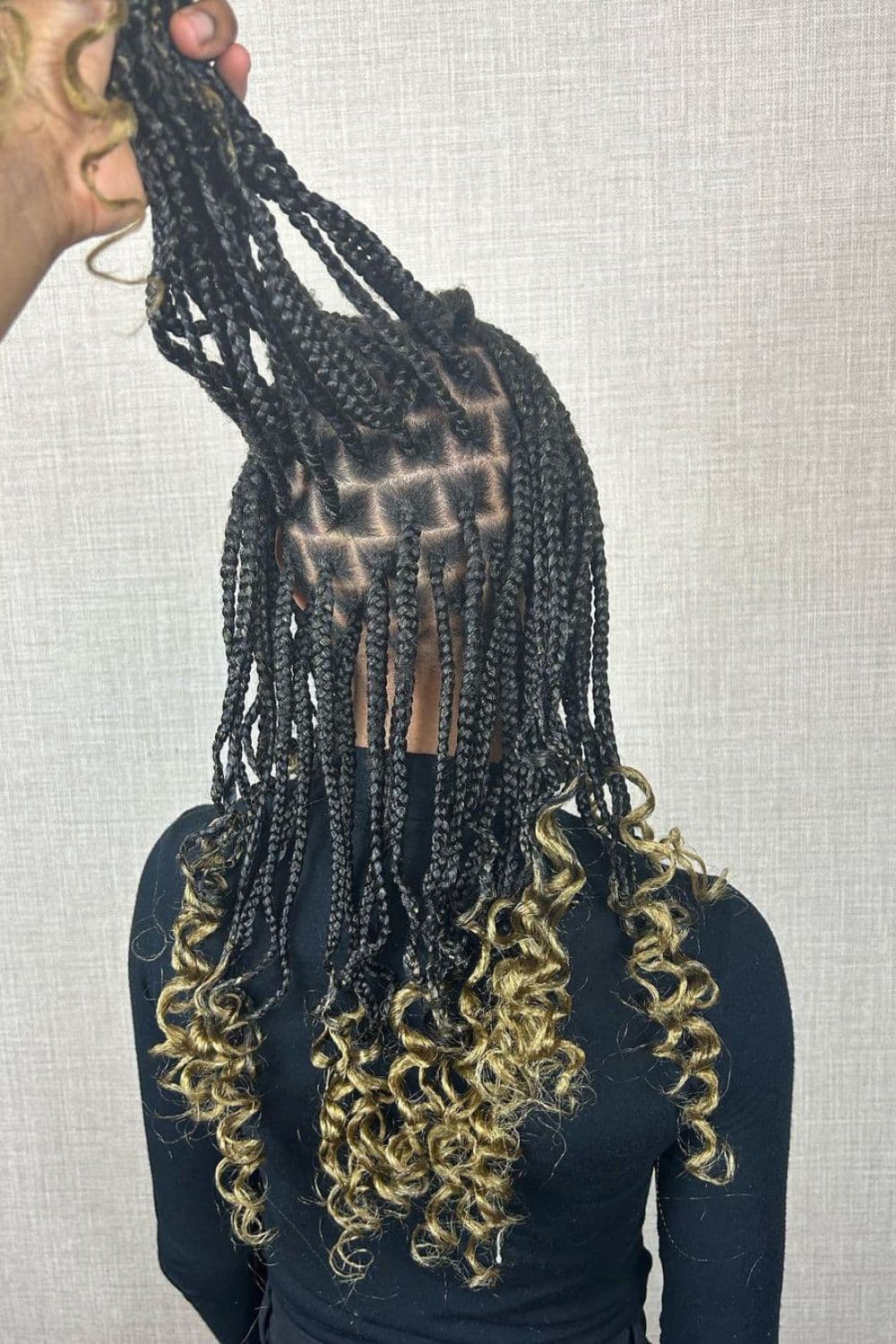 A woman wearing black long sleeves with black medium knotless box braids and blonde curly ends.