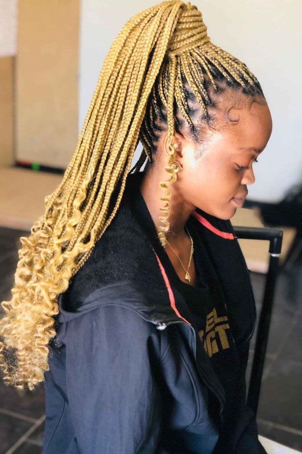 Side view of a woman with blonde medium knotless braids with curly ends in a high ponytail.