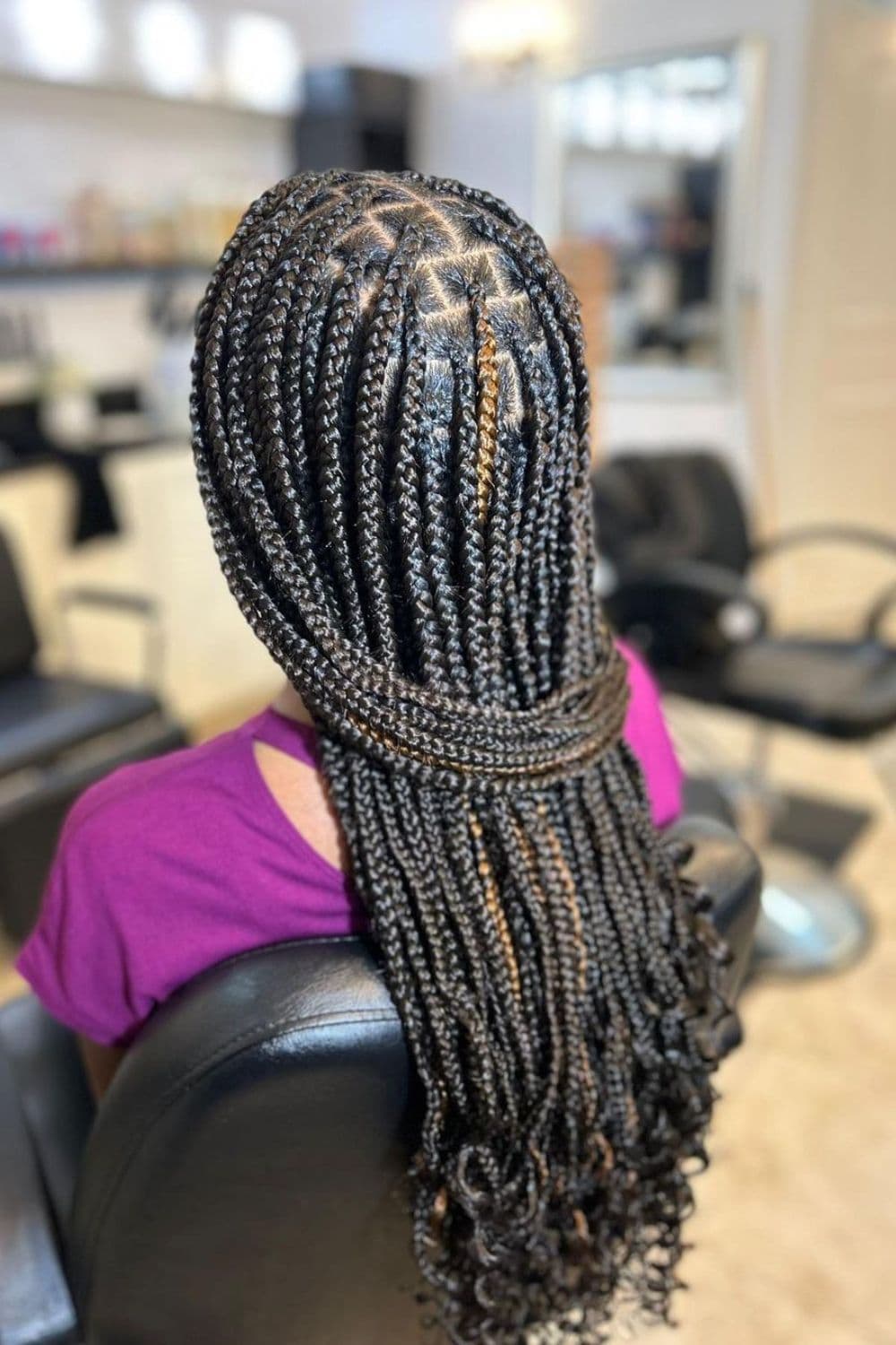 A woman sitting in a salon with black medium knotless braids with highlights.