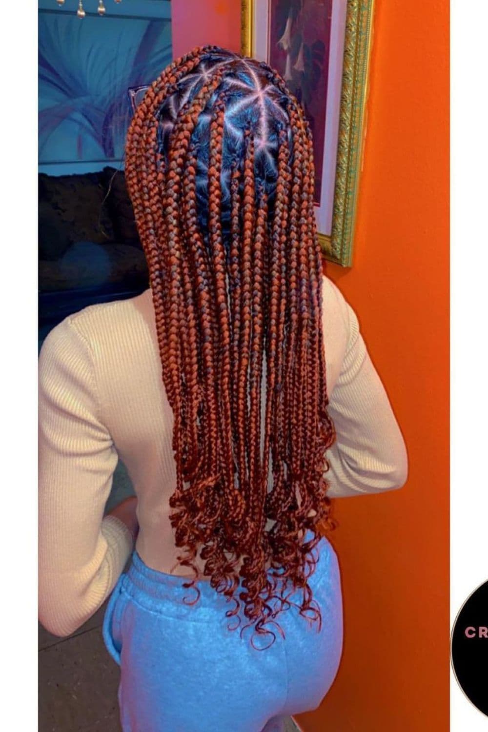 A woman standing with red medium knotless triangle braids with curly ends.