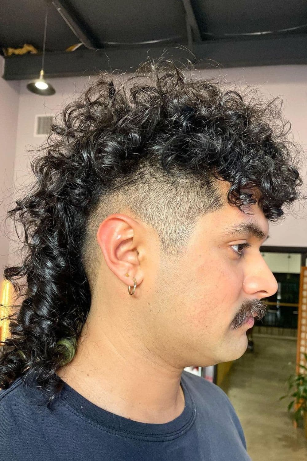 Side view of a man with mid-length curly mullet and a mustache.