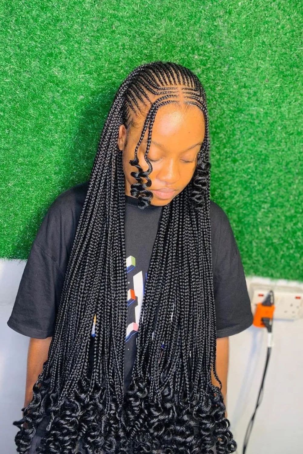 A woman wearing a black t-shirt with middle part tribal braids with curly ends.