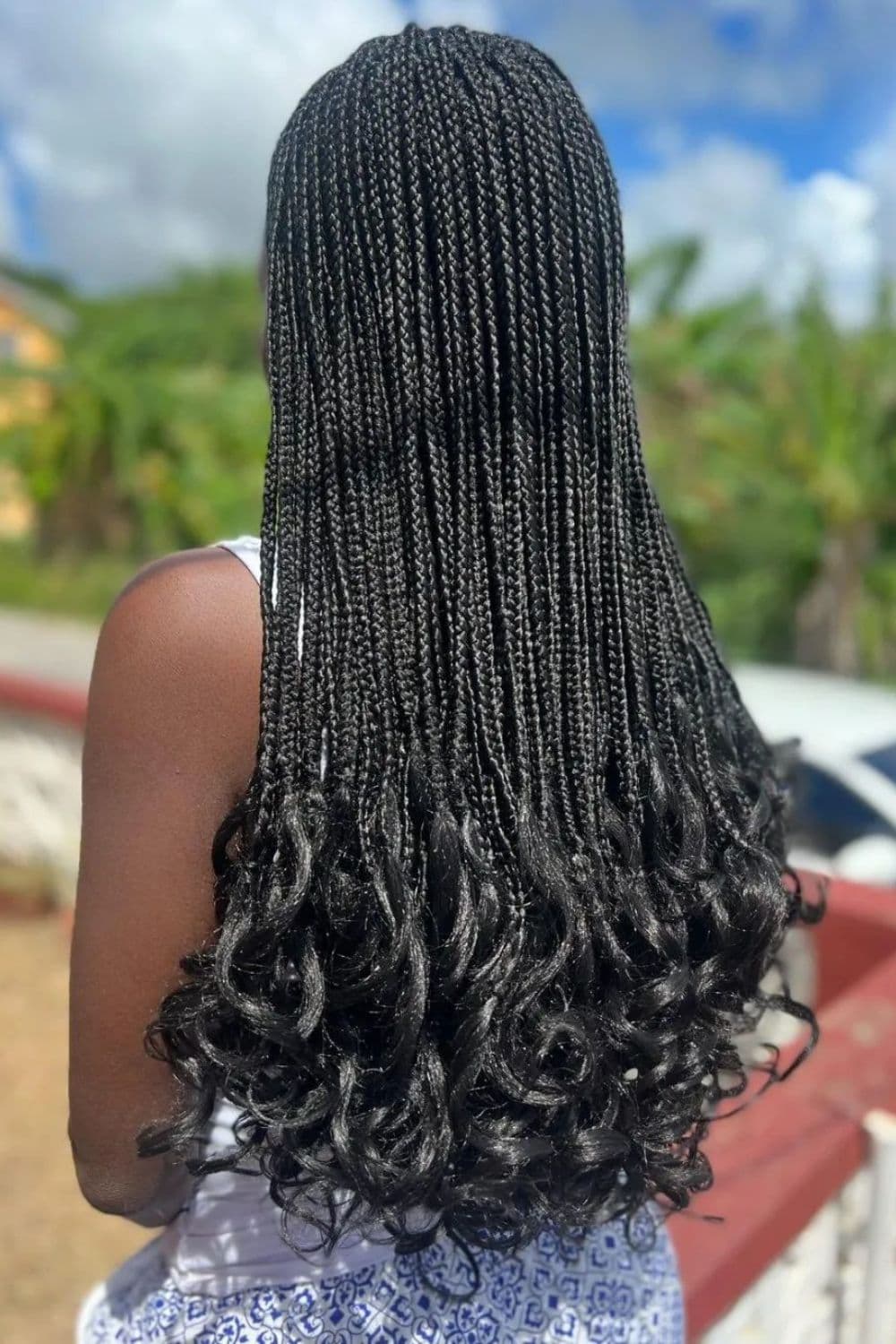 A woman with black mini braids with curly ends is standing outdoors.