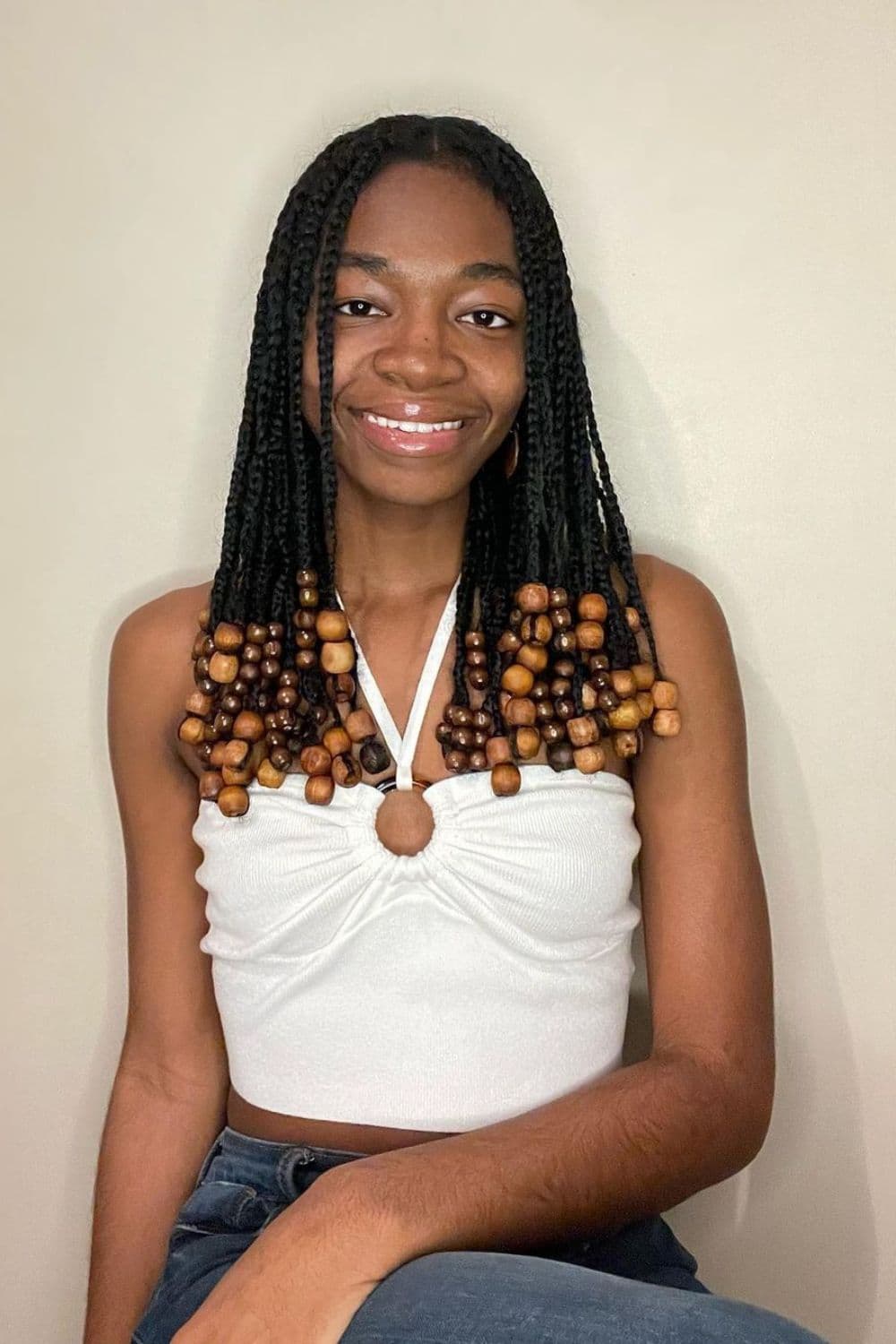 A woman wearing a white halter crop top with black mini braids with wooden beads.