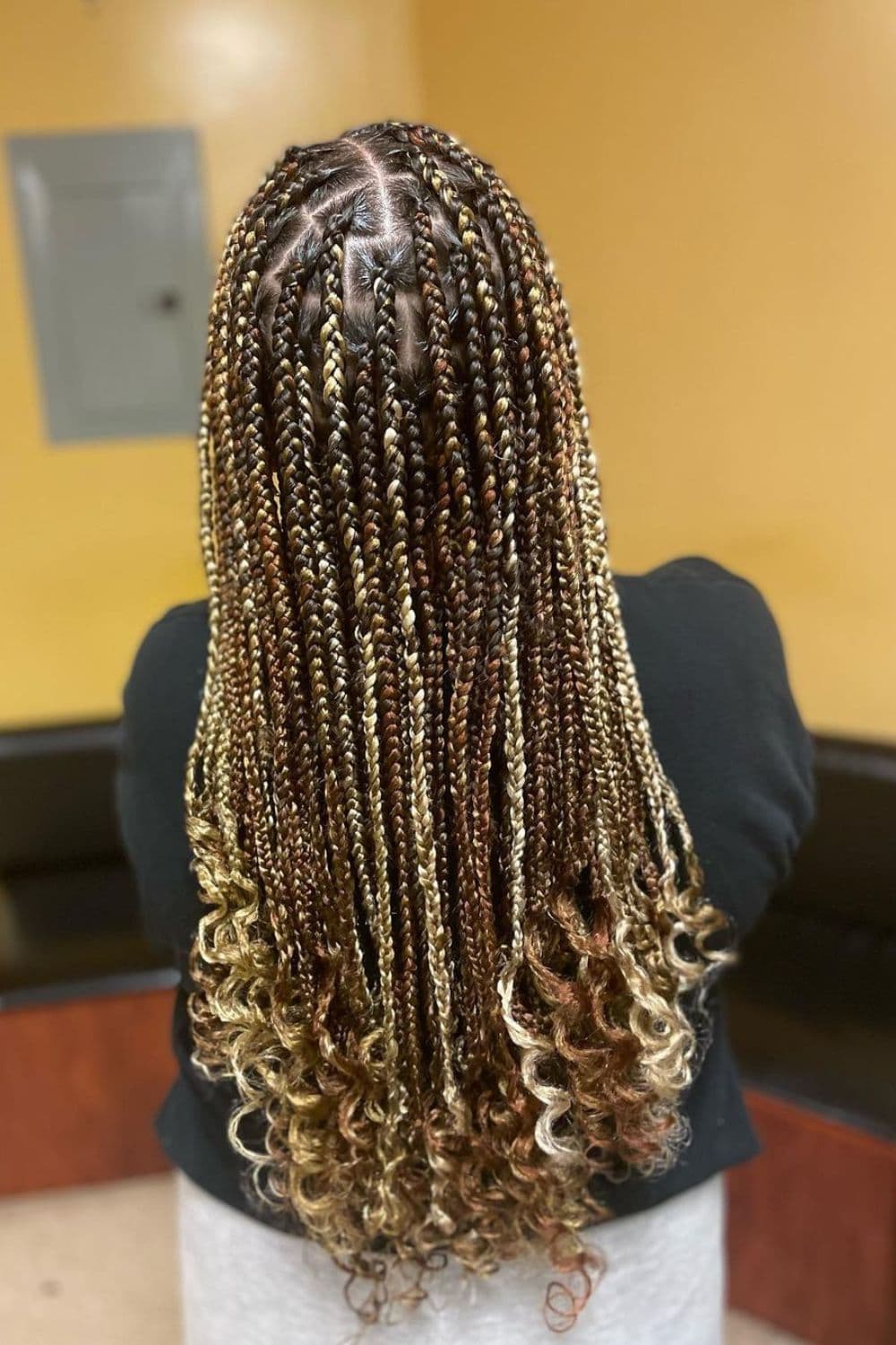 A woman standing with brown, black, and blonde medium knotless braids with curly ends.