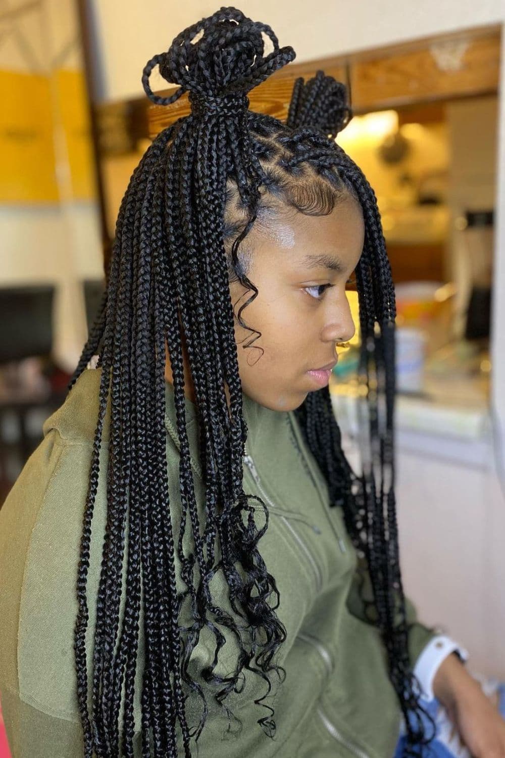 Side view of a girl with black medium knotless braids with curly ends and two buns.