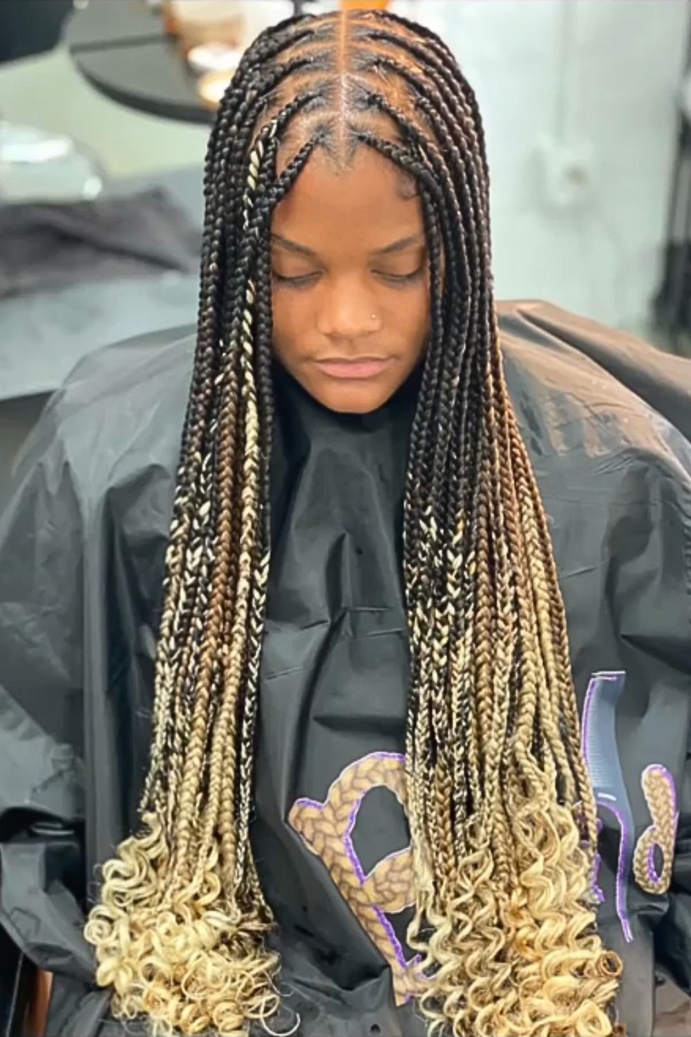 A woman sitting in a salon with blonde ombre knotless braids with curly ends.