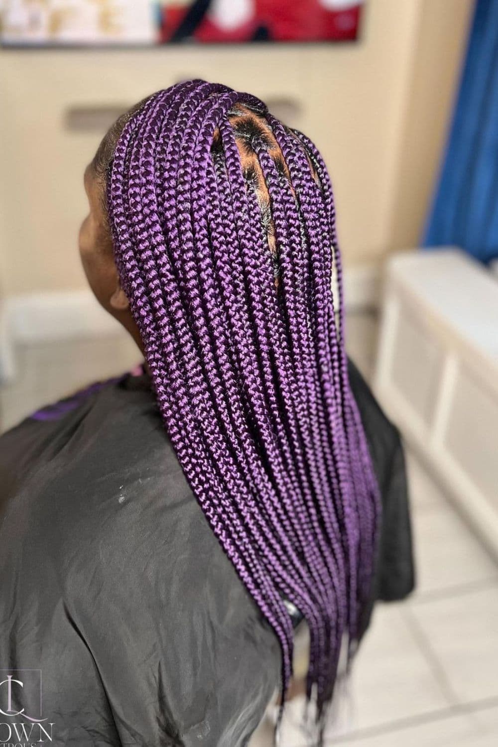 A woman sitting in a salon with purple knotless braids.