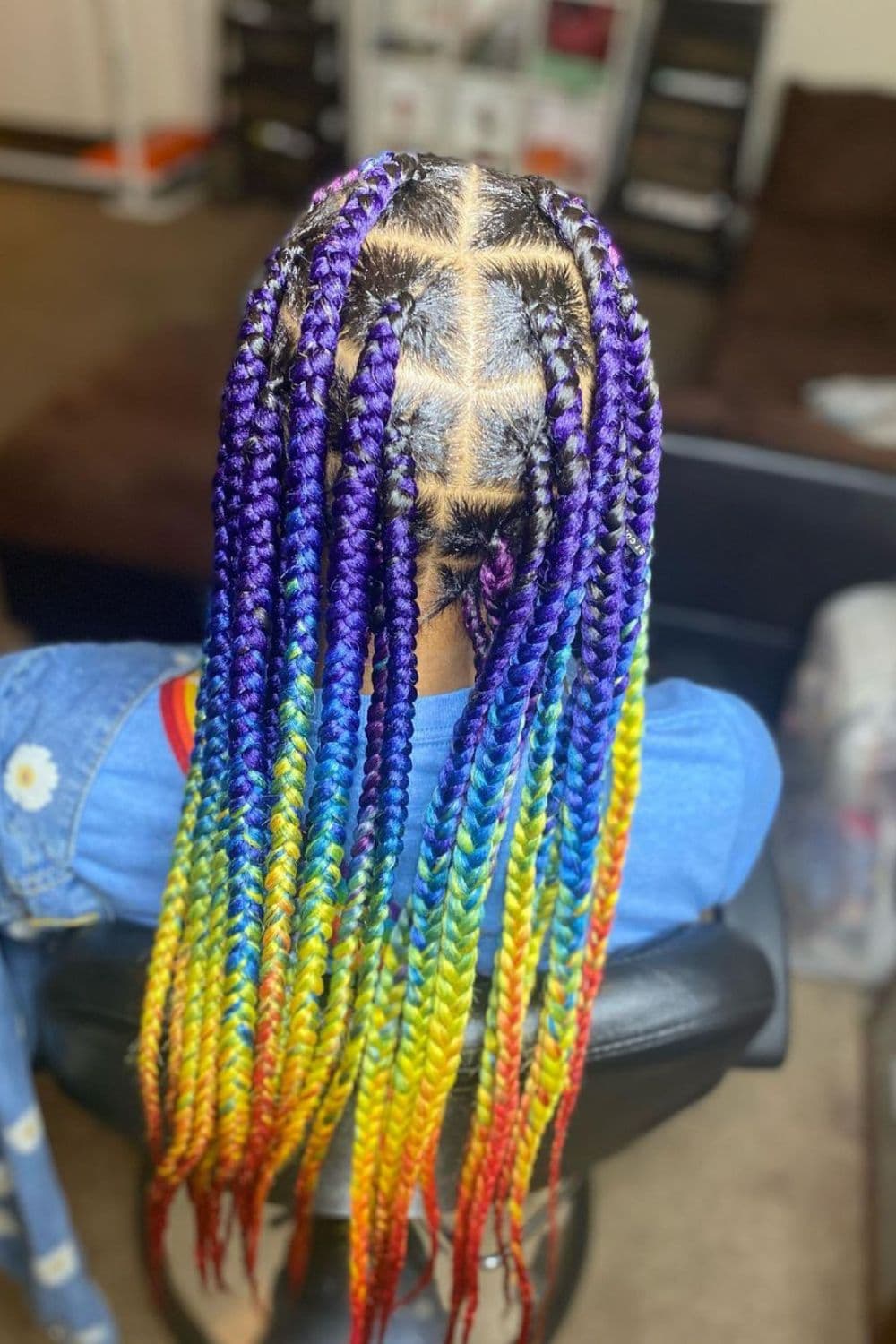 A woman sitting in a salon with rainbow knotless braids.