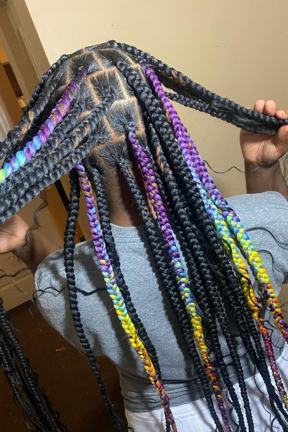 A girl holding her hair with rainbow or multicolored medium knotless braids.