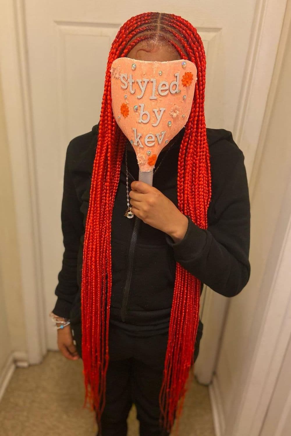 A woman standing covering her face with red middle-parted tribal braids.