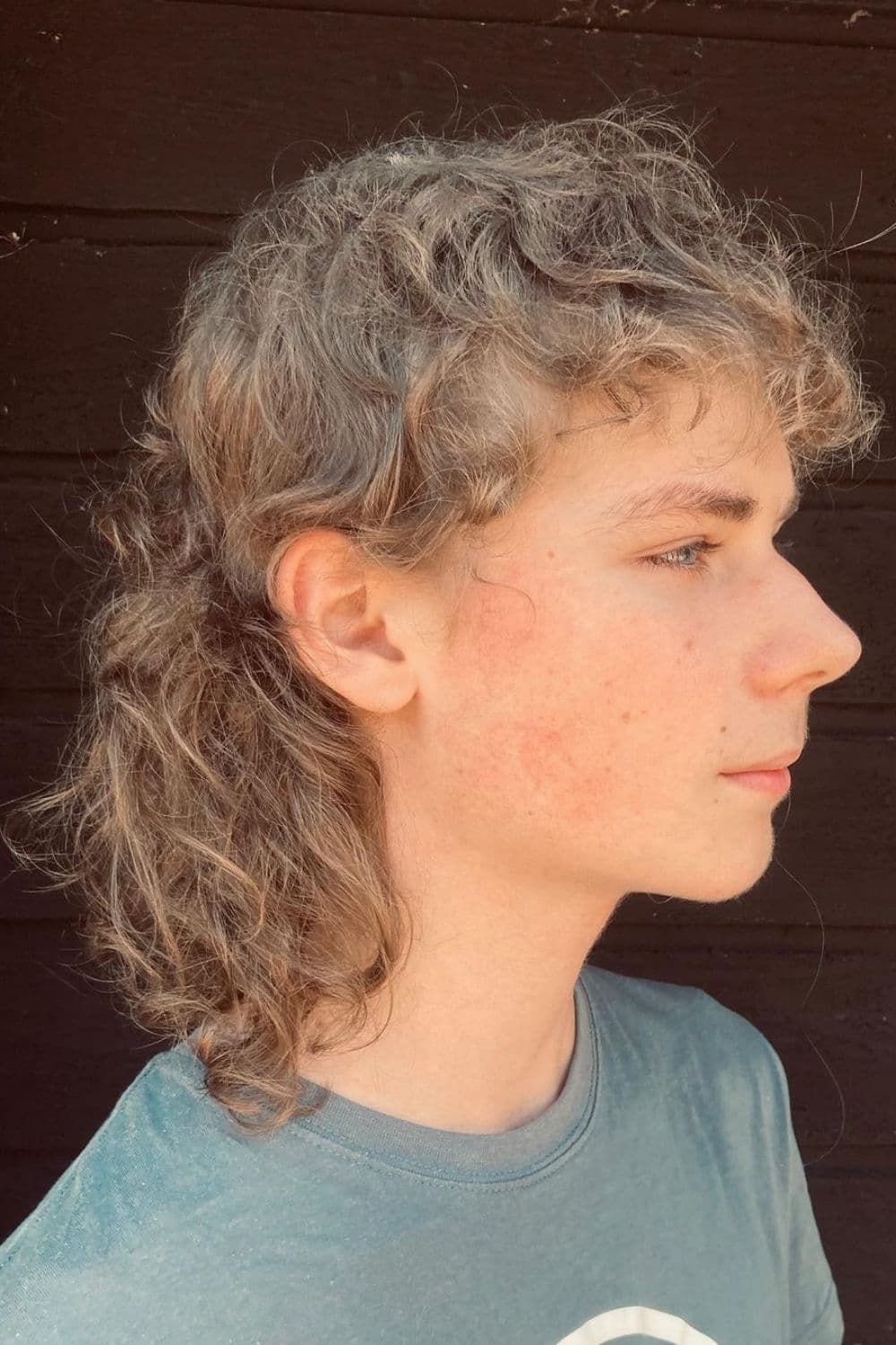 Side view of a man with shaggy curly mullet.