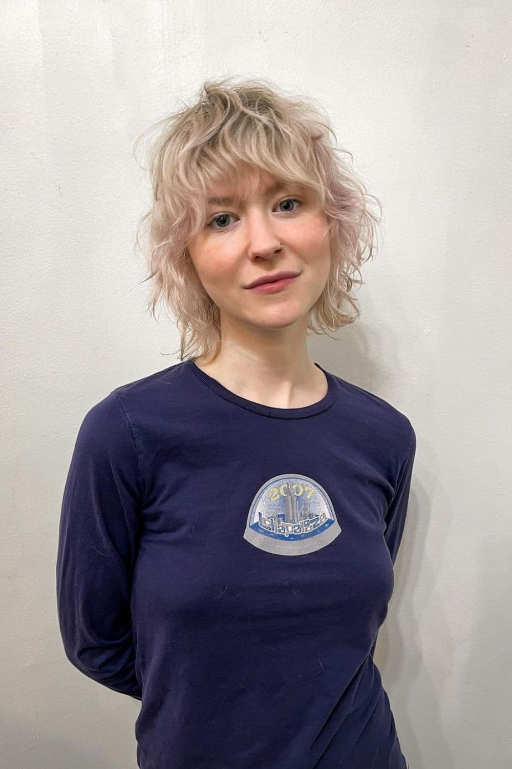 A woman wearing a purple long sleeve with a blonde short wavy wolf cut.