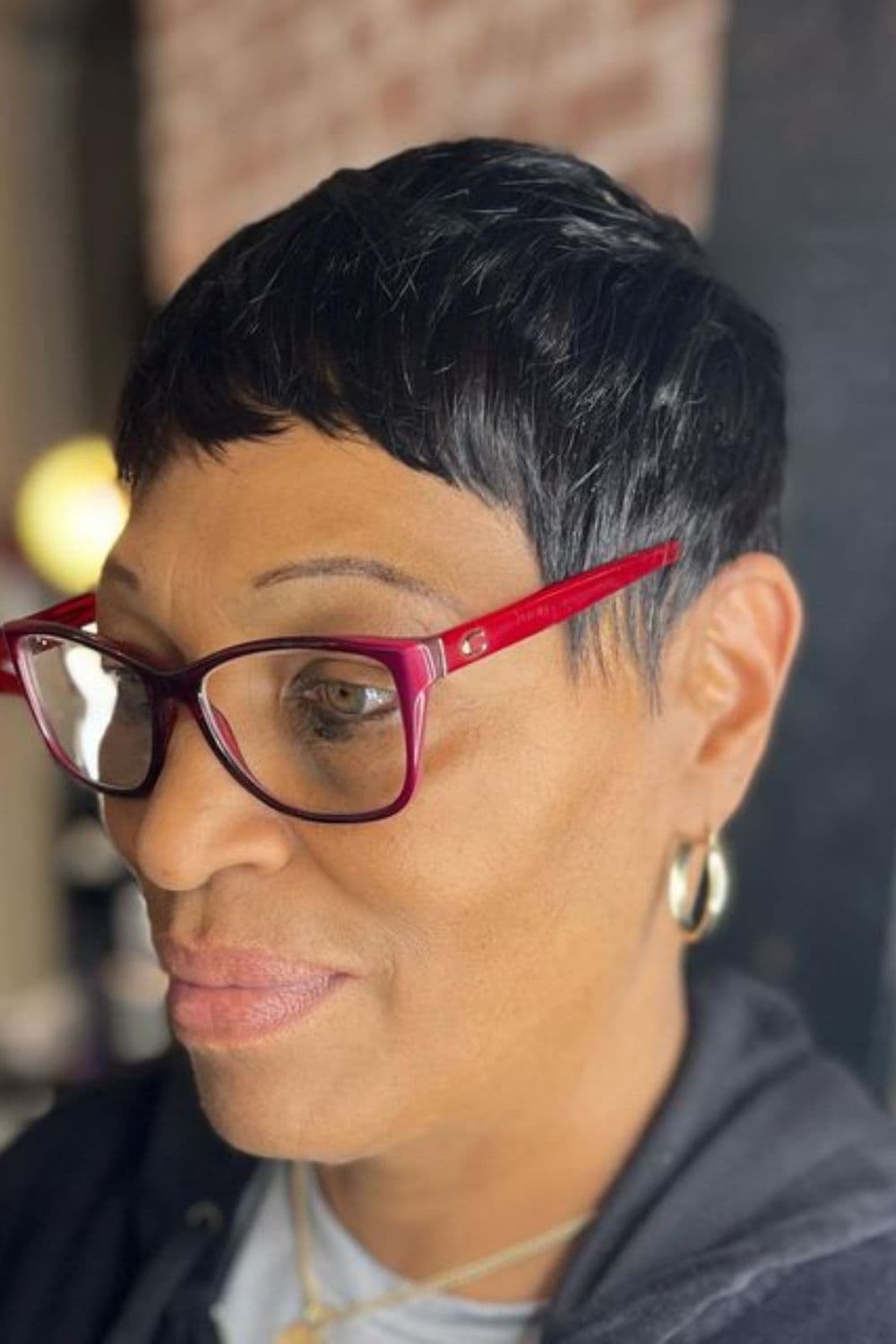 Side view of a woman wearing red eyeglasses with short weave with bangs.