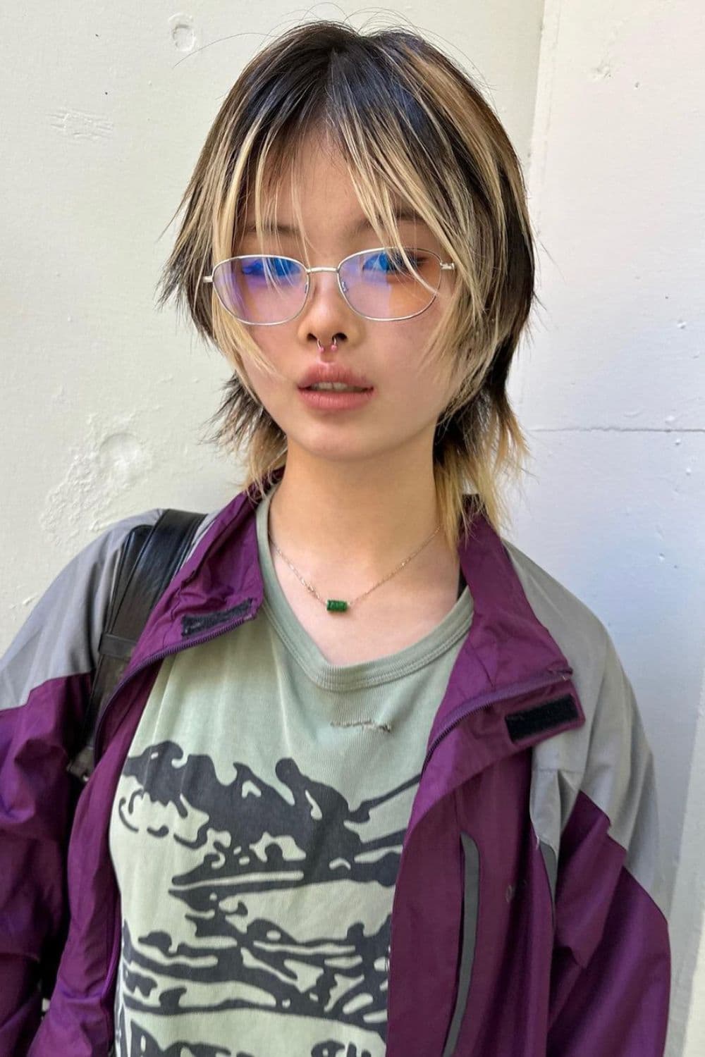 A woman wearing eyeglasses with a thin, black and blonde short wolf cut.