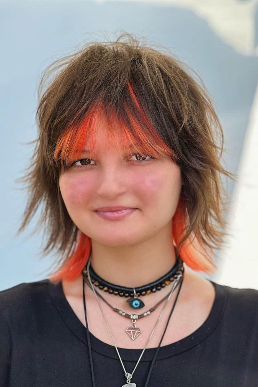A woman with a short wolf cut with orange-dyed bangs.