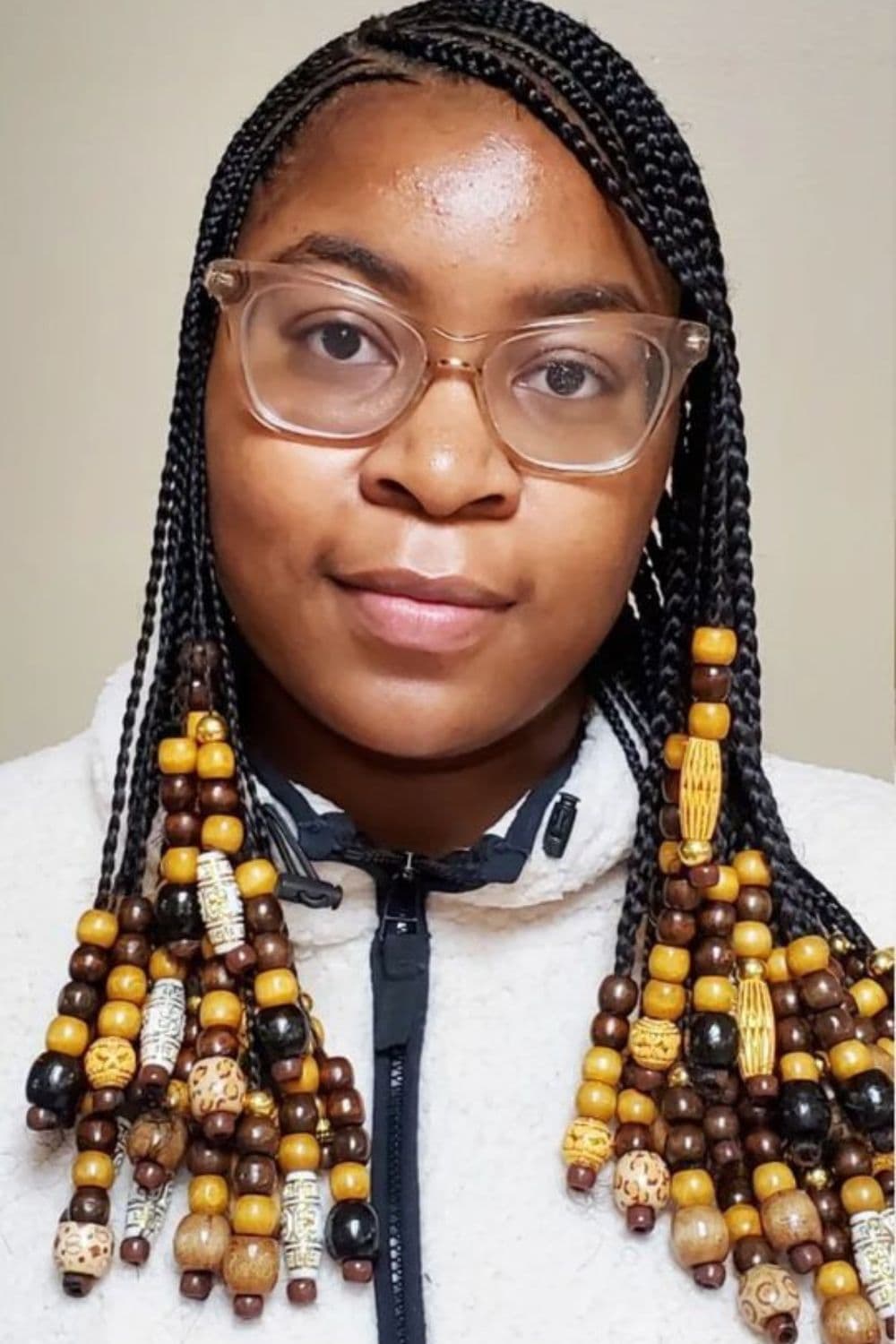 A woman wearing eyeglasses with side-part cornrows with beads.