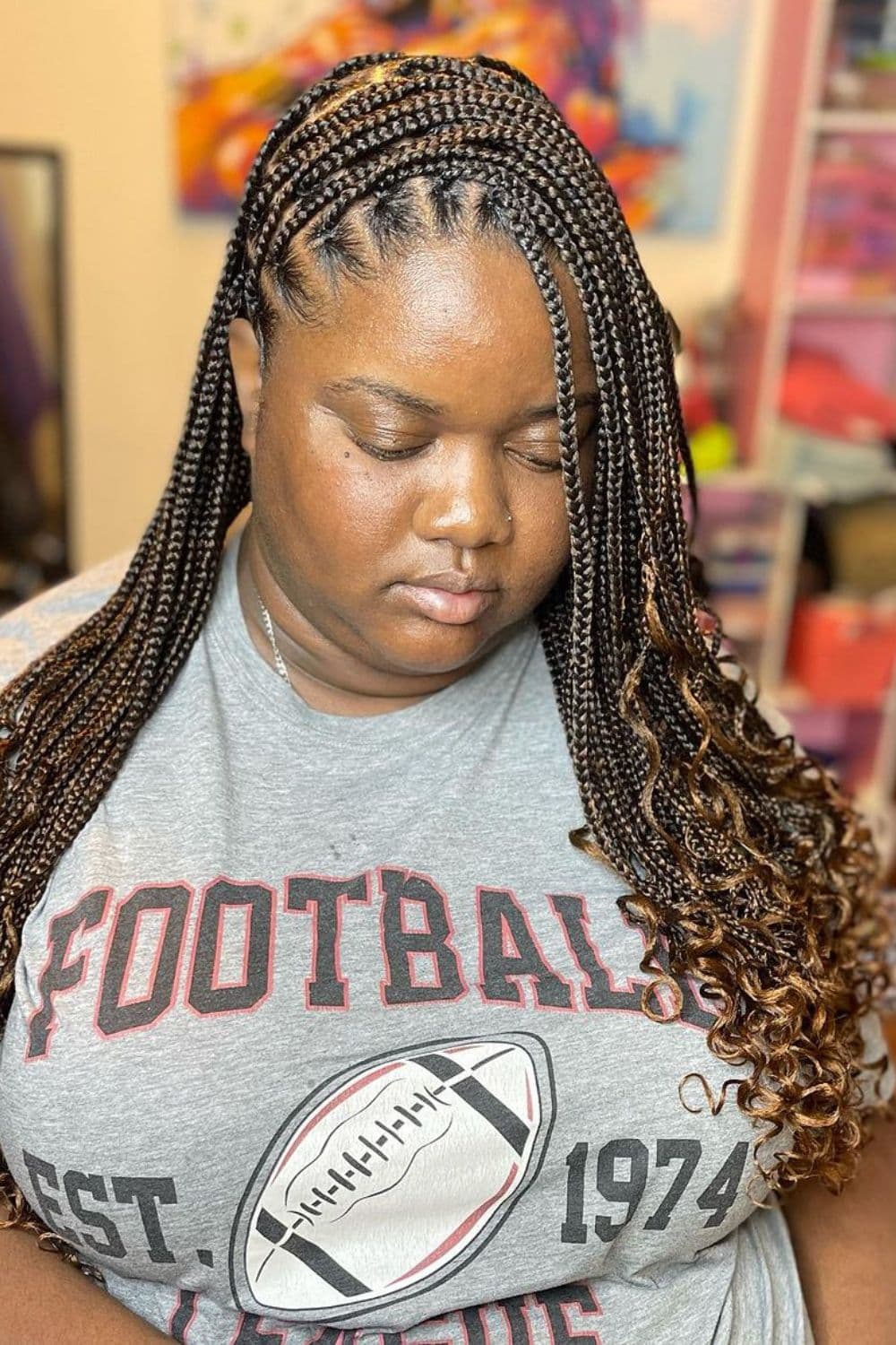 A woman wearing a gray t-shirt with side part brown medium knotless braids with curly ends.