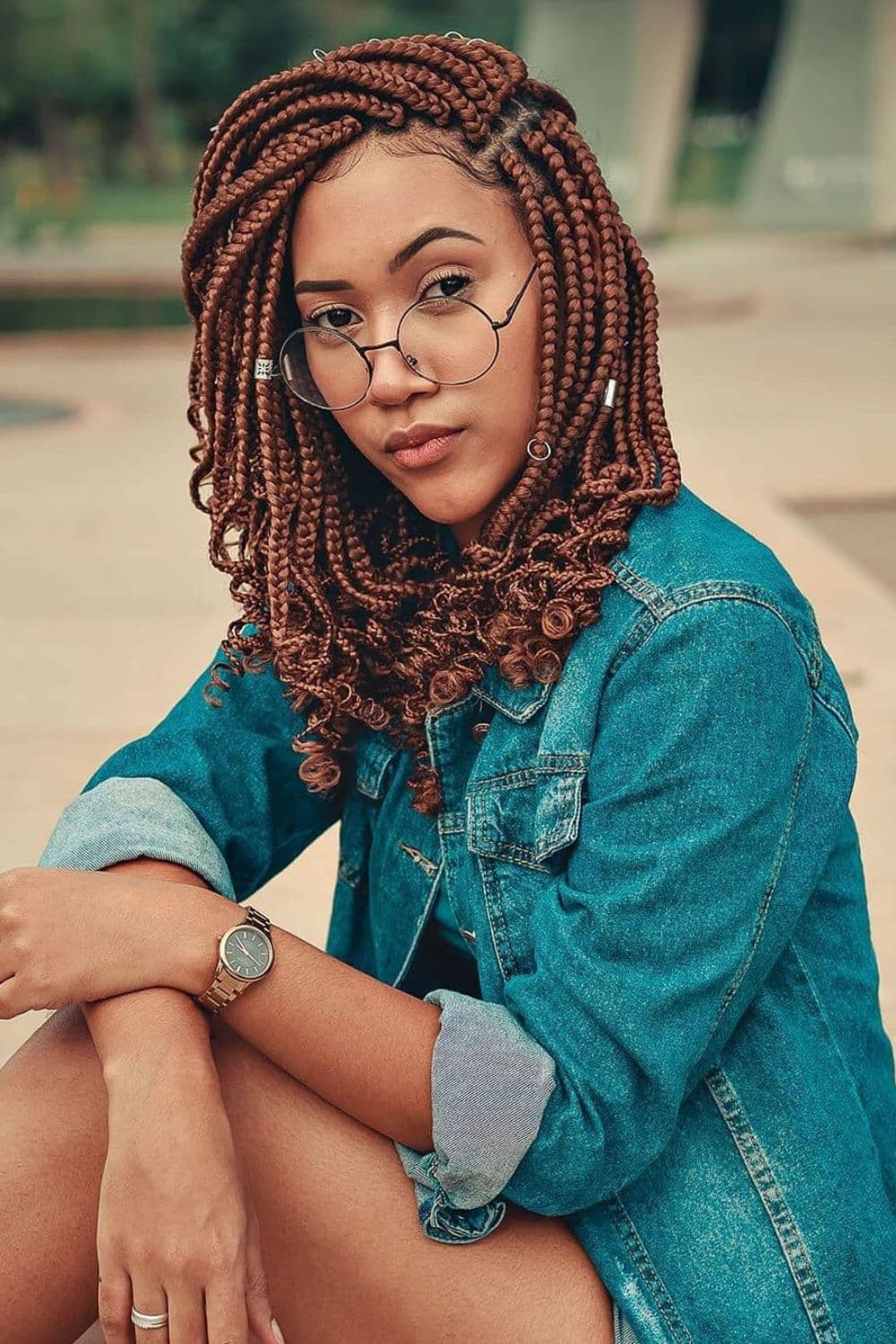 A woman in a denim jacket with brown side-part box braids with curly ends.