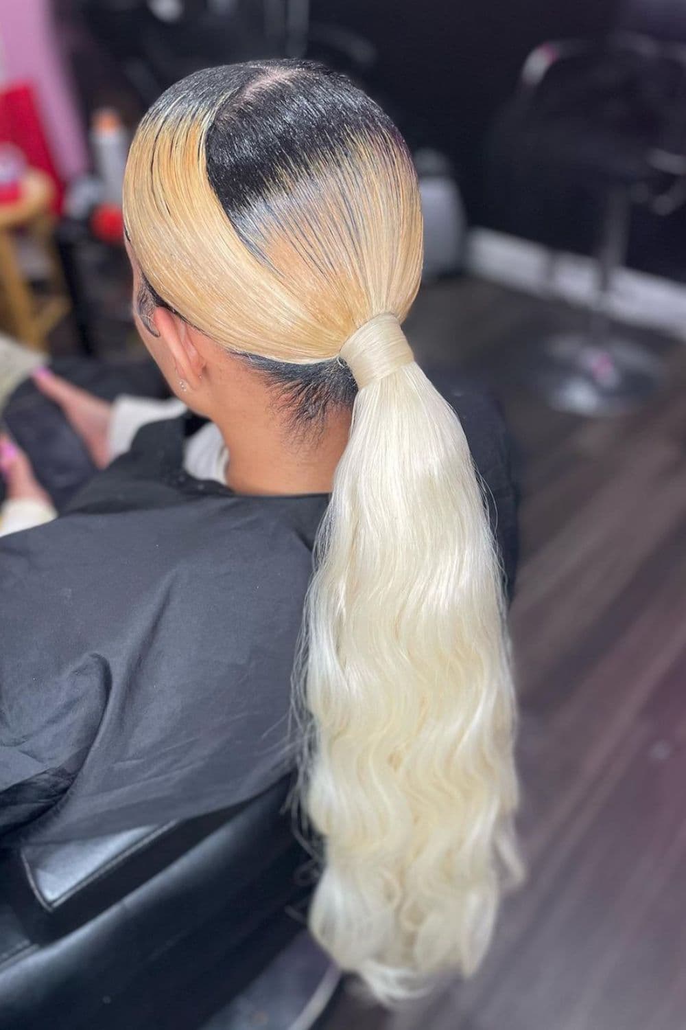 A woman sitting with a blonde sleek low ponytail.