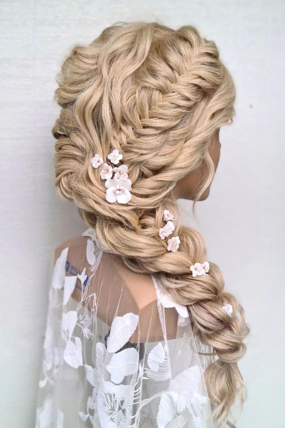 Side view of a mannequin with a sleek side French fishtail braid with flower accessories.