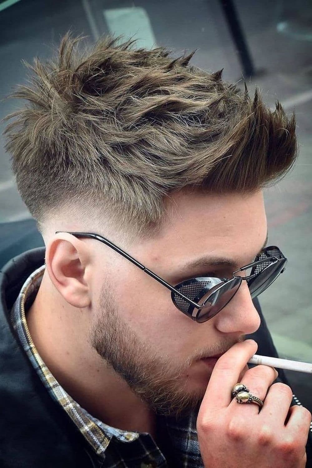 A man with spiky low taper fade and wearing sunglasses is holding a cigarette.