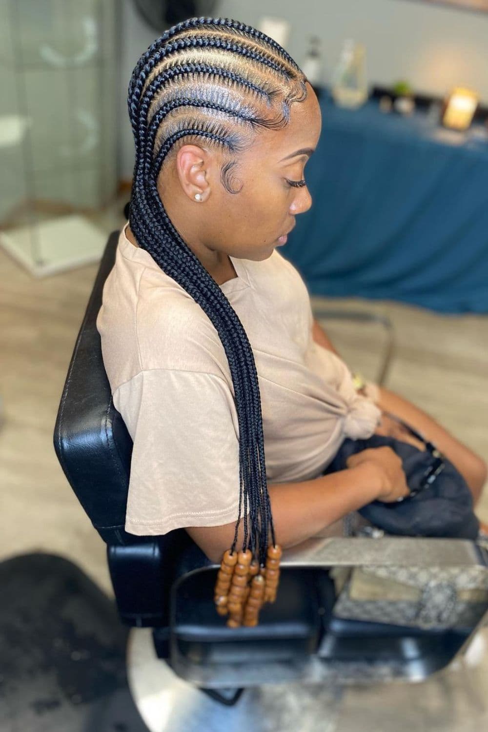 A woman sitting in a salon with stitch cornrows with beads.