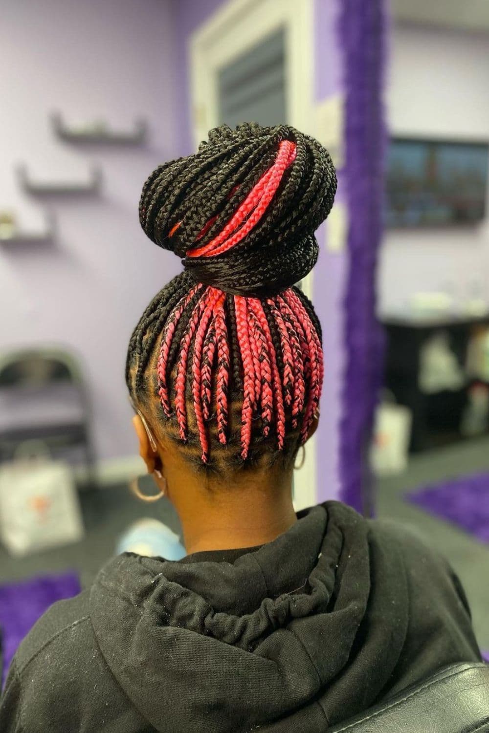 A woman with black and pink two-tone medium knotless braids in a bun.