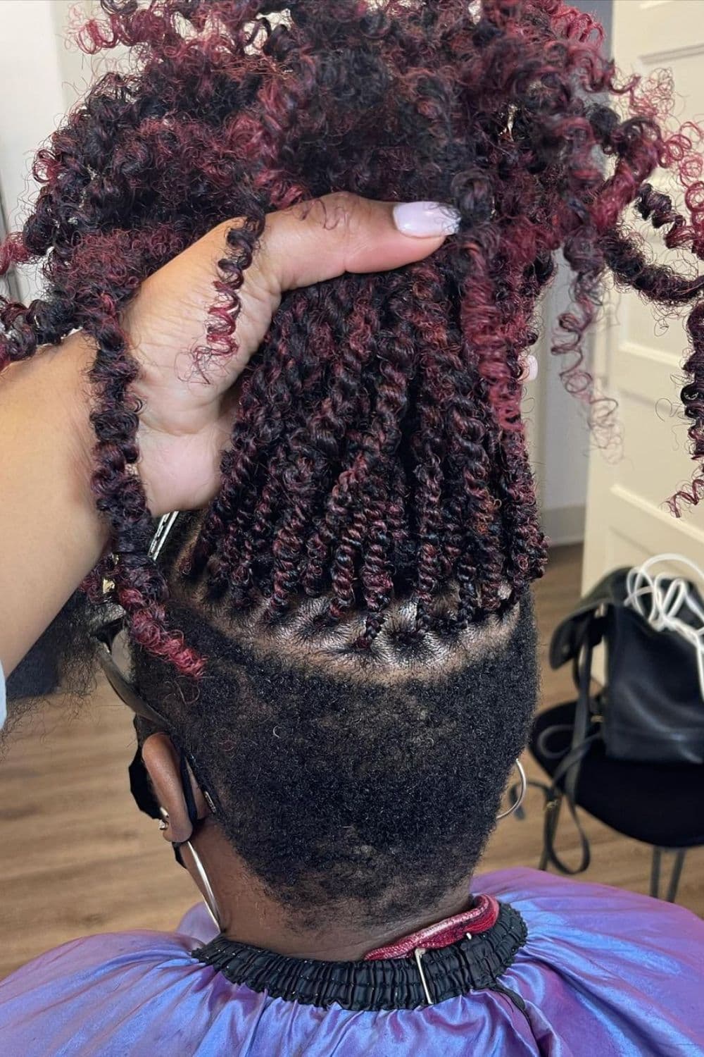 A woman with a black and red undercut passion twists and a woman's hand holding her hair up.