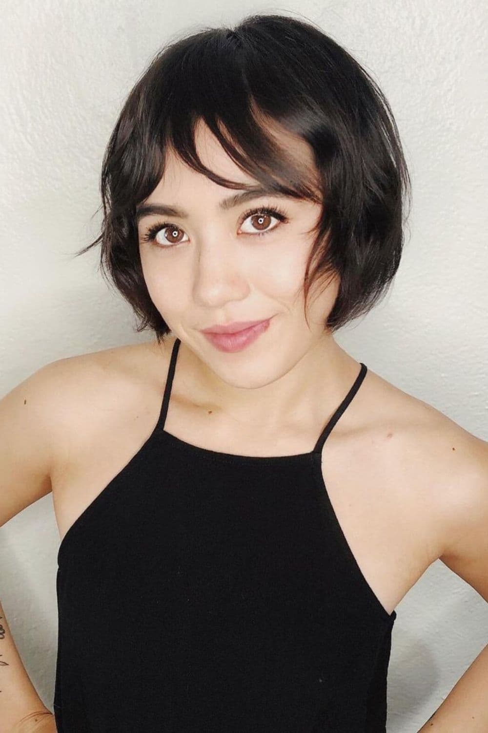 A woman wearing a black tank top with black wavy bob with face-framing pieces.