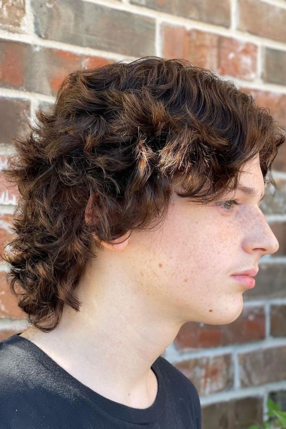 Side view of a man with a brown curly wolf cut.