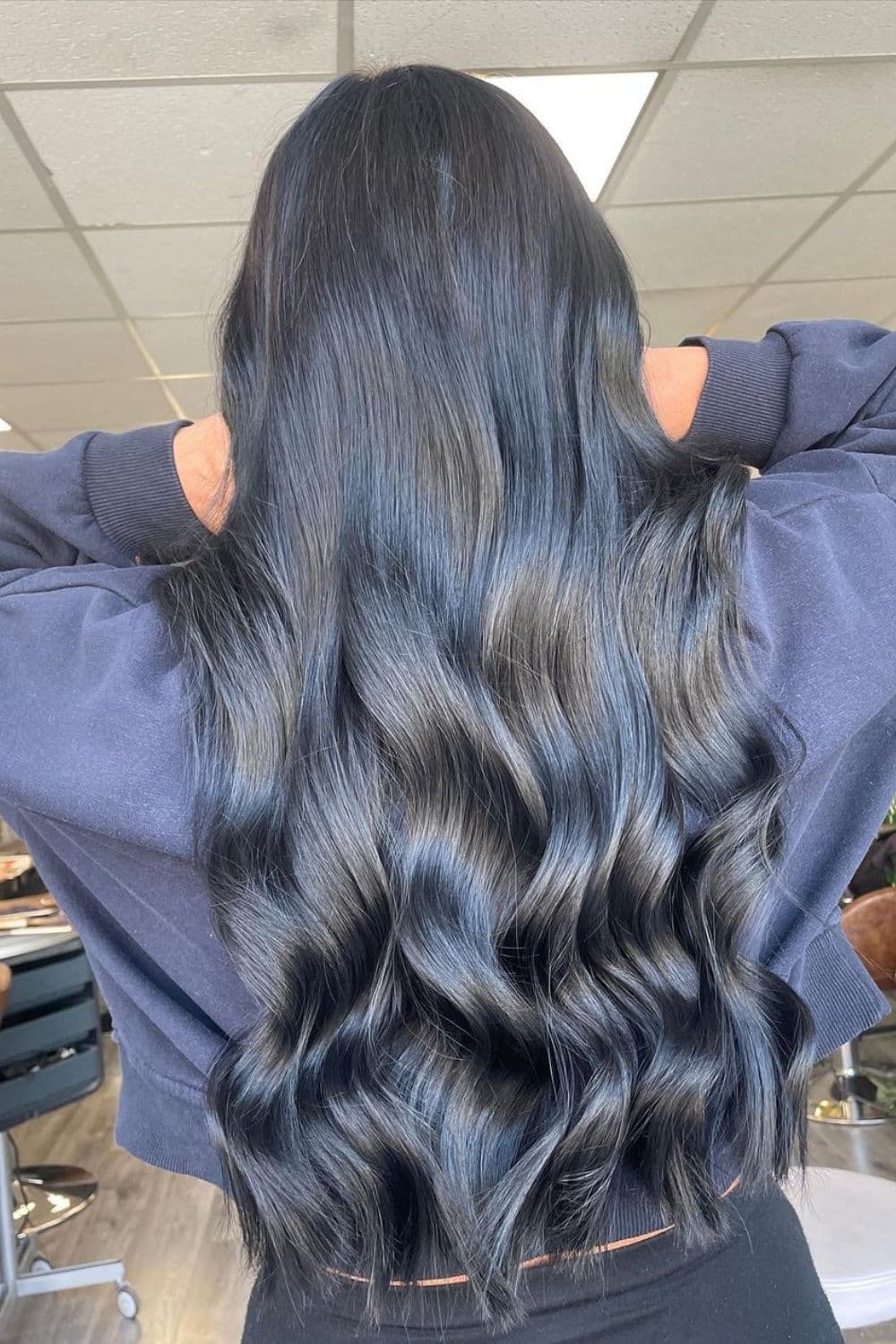 A woman with long blue black gloss hair with beach waves.