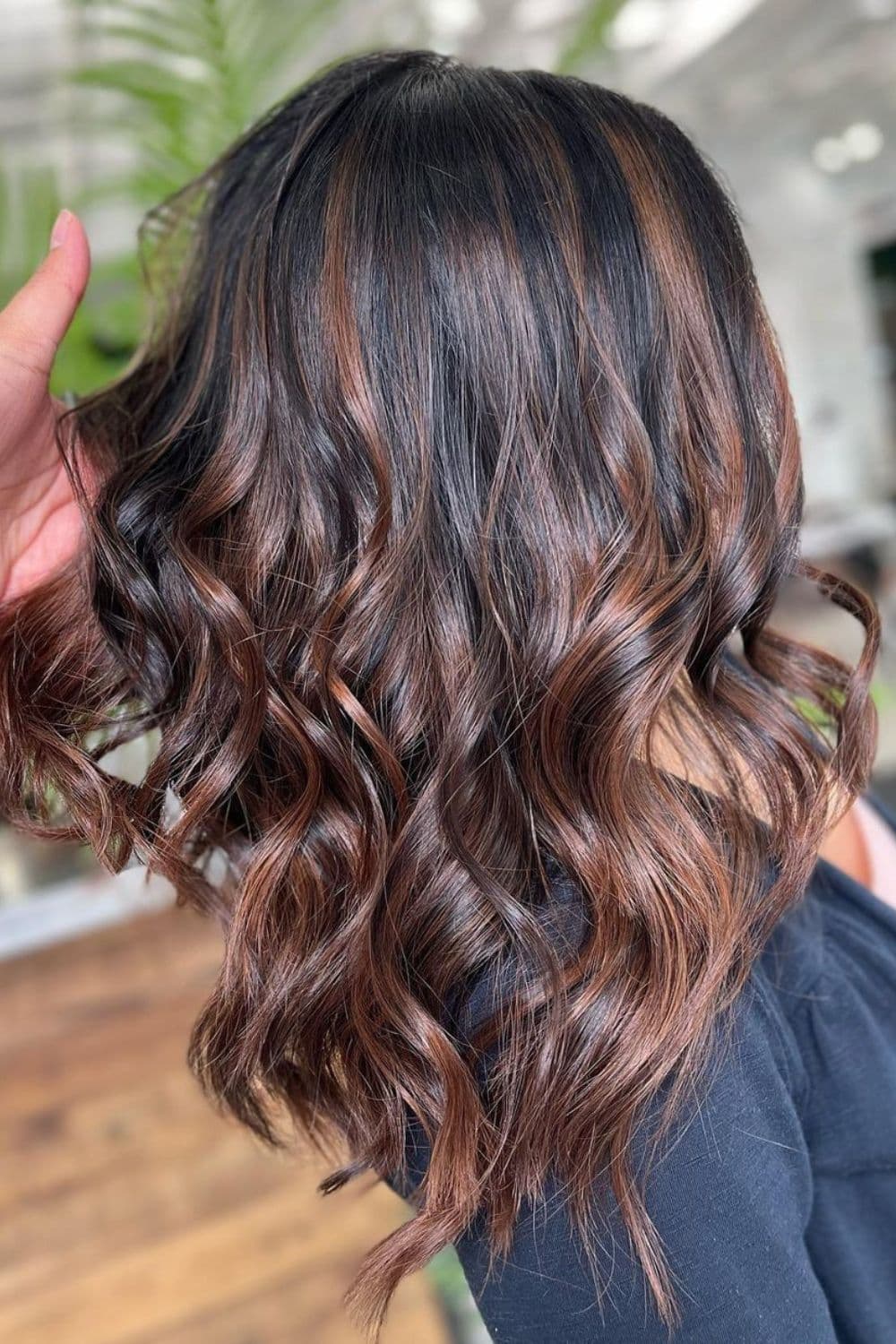 A woman with medium-length cherry chocolate balayage with curls.