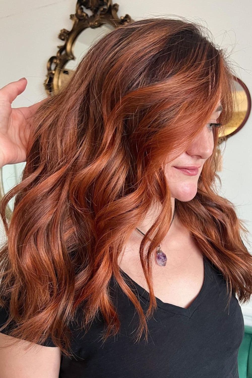 A woman with long copper balayage with big curls.