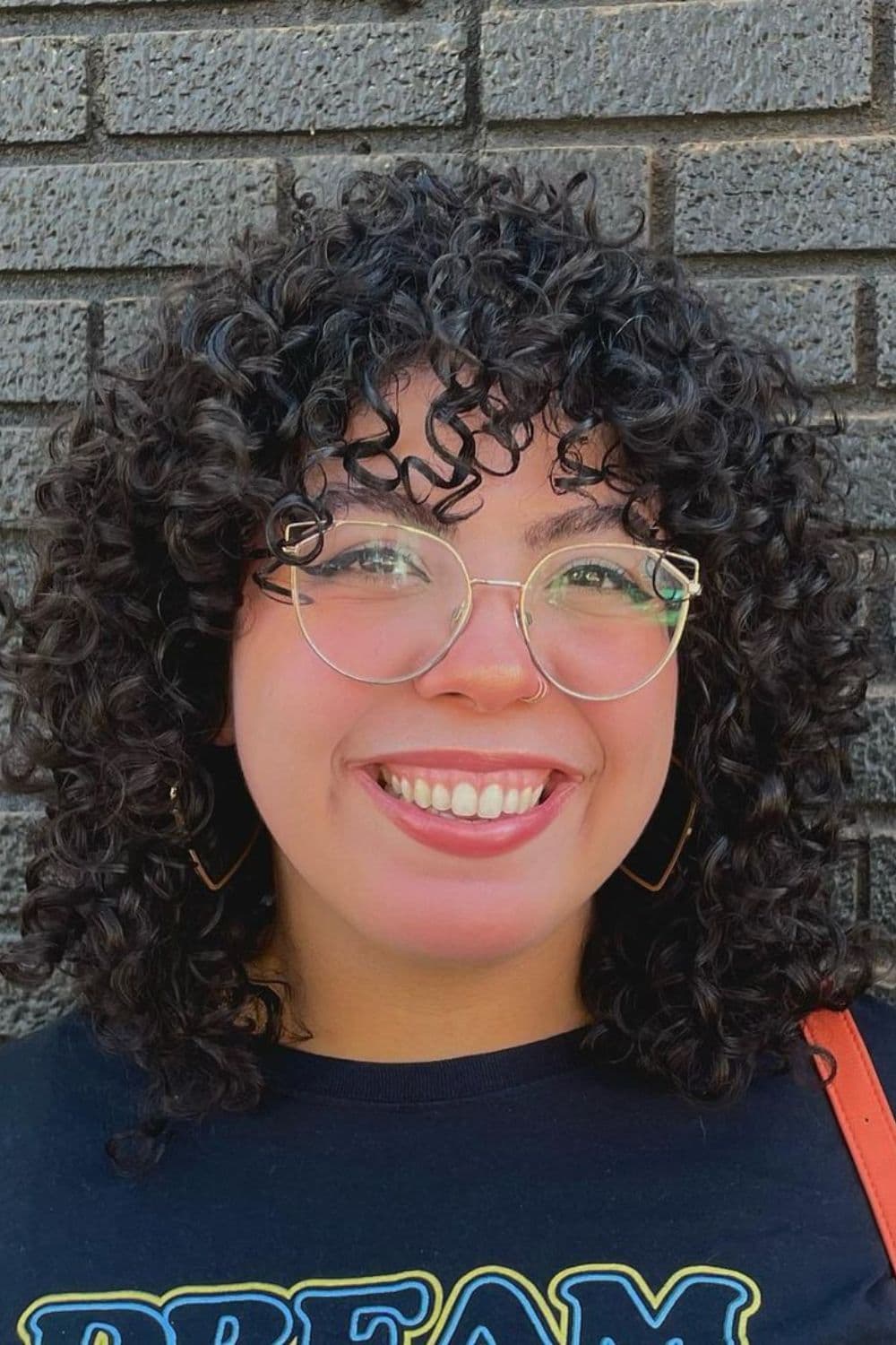 A woman with a black curly hair and curly bangs.