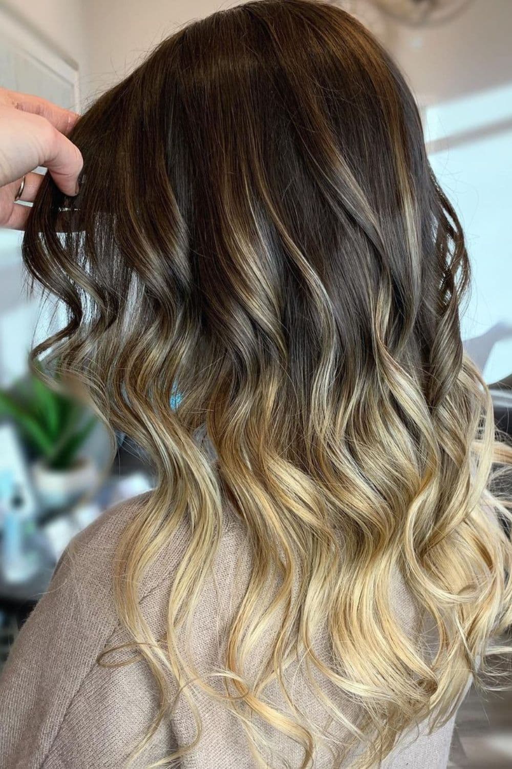 A woman with long dark brown hair to blonde ombre with curls.
