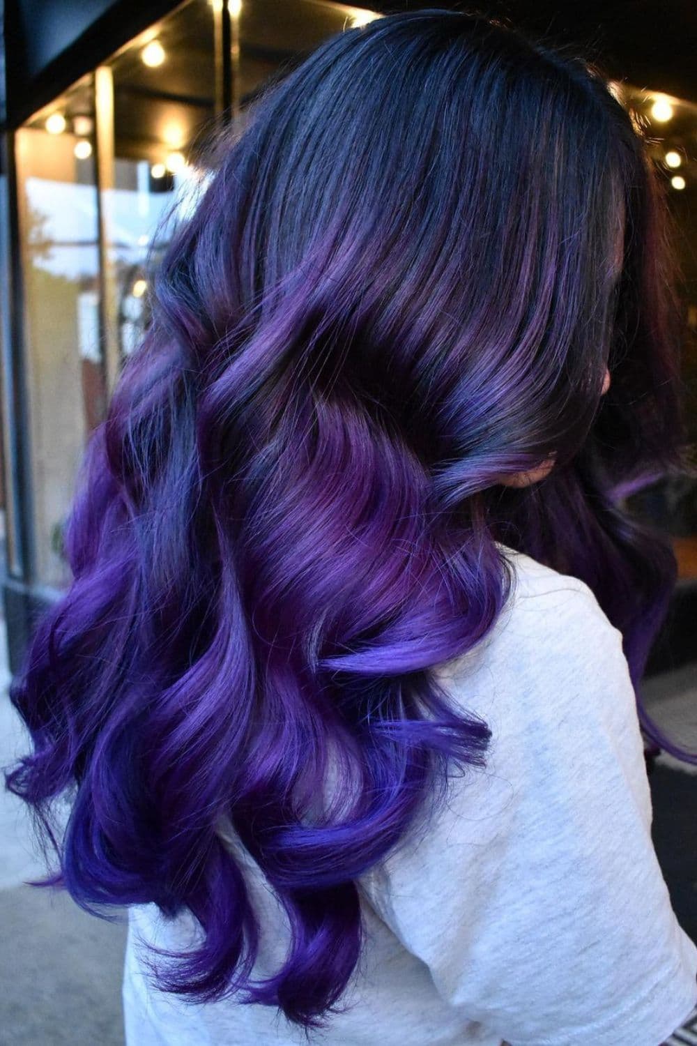 A woman with long deep purple balayage with big curls.